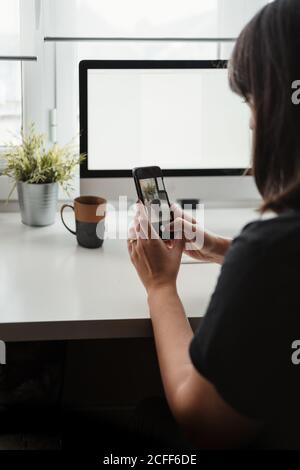 Crop blogger femmina senza volto scattando foto di spazio di lavoro mentre si siede A tavola con computer in ufficio a Parigi Foto Stock