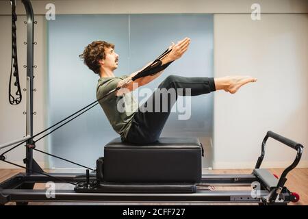 Vista laterale dello sportivo in activewear con pilates machine e. bracci allunganti con bande di resistenza Foto Stock