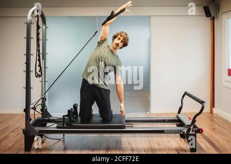 Sportivo in activewear utilizzando pilates macchina e bracci di allungamento con bande di resistenza Foto Stock