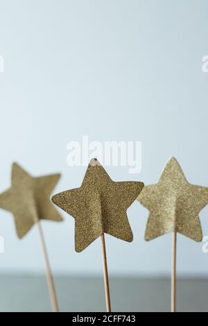 Stelle dorate brillanti e creative su bastone sottile per la decorazione delle vacanze su sfondo grigio Foto Stock