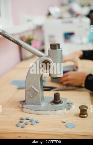 Crop persona anonima mani tirando la leva del costruttore di pulsanti su tavolo in laboratorio professionale di vestiario mentre si fa l'indumento Foto Stock