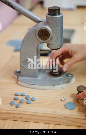 Crop persona anonima mani tirando la leva del costruttore di pulsanti su tavolo in laboratorio professionale di vestiario mentre si fa l'indumento Foto Stock