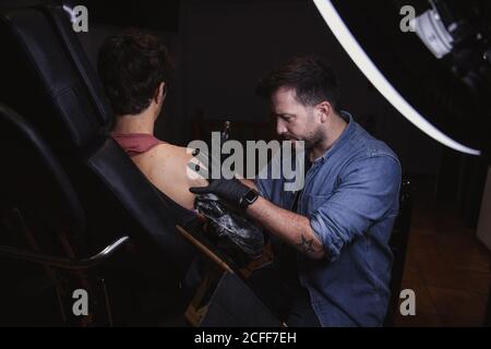 Master facendo tatuaggio sull'avambraccio del cliente maschile Foto Stock