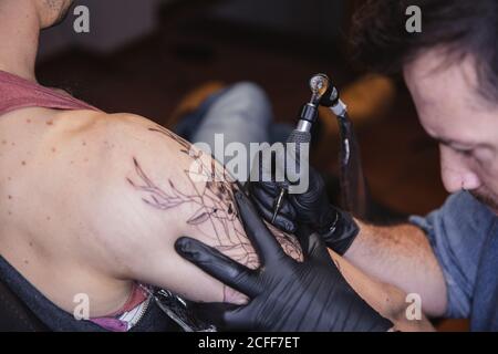Master facendo tatuaggio sull'avambraccio del cliente maschile Foto Stock
