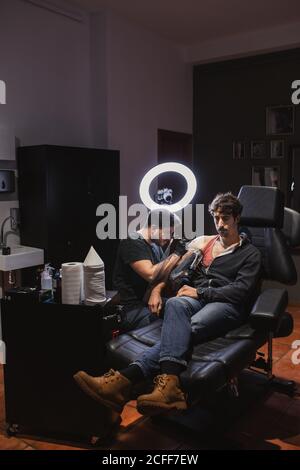 Master facendo tatuaggio sull'avambraccio del cliente maschile Foto Stock