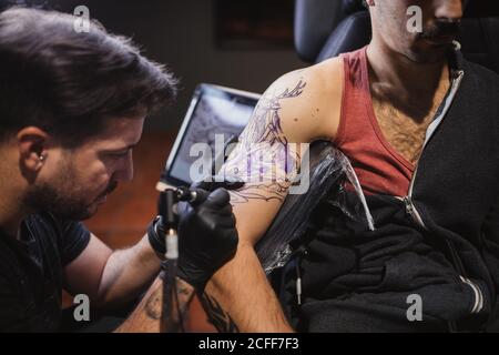 Master facendo tatuaggio sull'avambraccio del cliente maschile Foto Stock