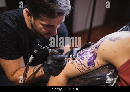 Master facendo tatuaggio sull'avambraccio del cliente maschile Foto Stock