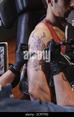 Master facendo tatuaggio sull'avambraccio del cliente maschile Foto Stock