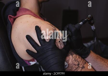 Master facendo tatuaggio sull'avambraccio del cliente maschile Foto Stock