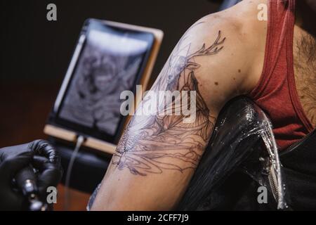 Master facendo tatuaggio sull'avambraccio del cliente maschile Foto Stock