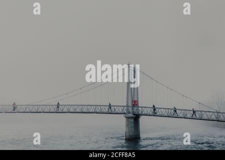 Persone che camminano attraverso il fiume sul ponte moderno con nebbia giorno nuvoloso Foto Stock