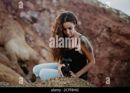 Viaggiatore femminile con macchina fotografica vintage seduto su ruvida scogliera rocciosa in natura Foto Stock