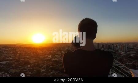 Silhouette di un fotografo che scatta foto sulla parte superiore del edificio al tramonto Foto Stock