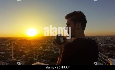 Silhouette di un fotografo che scatta foto sulla parte superiore del edificio al tramonto Foto Stock