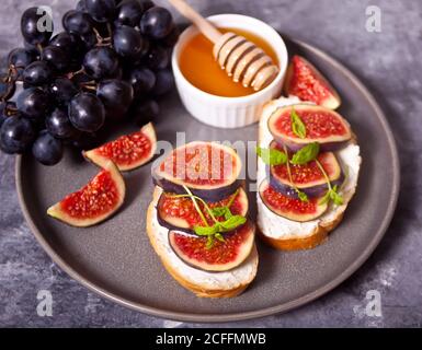 Sandwich con formaggio cremoso, fichi e miele servito sulla piastra grigia su fondo di cemento. Concetto di cibo sano Foto Stock