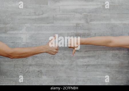 Mani forti abbronzate di uomo e donna di raccolto gesturing e mostrando pollice su e giù sullo sfondo della parete grigia Foto Stock