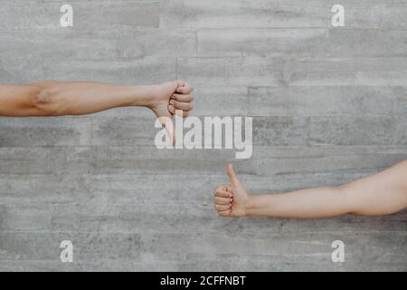 Mani forti abbronzate di uomo e donna di raccolto gesturing e mostrando pollice su e giù sullo sfondo della parete grigia Foto Stock