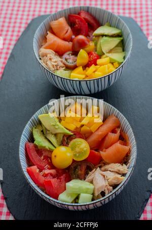 Ciotole con verdure fresche tritate e carne di salmone e. pollo messo a tavola in cucina per pranzo Foto Stock