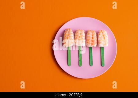 Vista dall'alto del set di sushi nigiri EBI con gamberi serviti a forma di pop-sicle e posti su piatto su sfondo arancione in studio Foto Stock