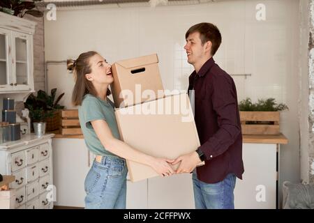 Vista laterale della giovane coppia che fa sforzo e trasporta il cartone scatole con roba in casa Foto Stock