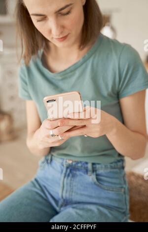 Giovane donna a piedi nudi che si rompe e comodamente seduto sulla lavatrice bianco surf telefono cellulare in cucina spaziosa Foto Stock