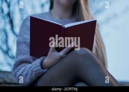 Vista ravvicinata della giovane donna freelancer in morbido jumper e camicia gonna nera che controlla il calendario nel blocco note mentre riposa su una panca di legno nel parco primaverile Foto Stock