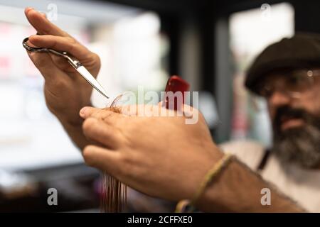 acconciatore uomo sfocato irriconoscibile che tiene le forbici e costumer di taglio a pettine capelli in un moderno barbiere Foto Stock