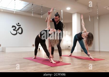 Equilibrate le donne calme e l'insegnante di uomo che aiutano a correggere la posa posizione laterale estesa sulla lezione di yoga Foto Stock