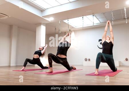 Vista laterale di donne calme equilibrate e l'uomo concentrato su allungare e alzare le mani in su in guerriero una postura sopra lezione di yoga Foto Stock