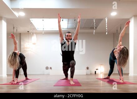 Le donne e l'uomo calmi e equilibrati si concentravano sullo stretching e sull'innalzamento mani in su in guerriero una postura e l'angolo laterale esteso mettiti in posa per una lezione di yoga Foto Stock