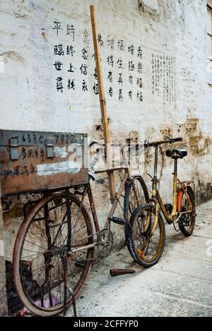 Coppia di shabby bici appoggiate su muro di pietra con disegnato Geroglifici vicino al tempio della città di Hong Kong Foto Stock