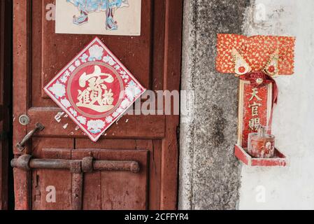 Esterno della porta di legno con foto di geroglifico con rosso Piccolo santuario appeso al muro di casa residenziale a Hong Kong Foto Stock