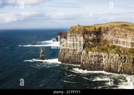 Maestosa vista di ruvide e alte scogliere sulla riva del mare Irlanda con le onde oceaniche che si infrangono Foto Stock