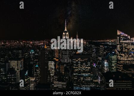 Vista aerea di megalopoli con pareti di vetro illuminate e futuristico facciate di alti grattacieli sullo sfondo in serata Foto Stock