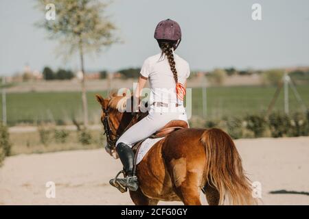 Vista posteriore di anonimo fantino ragazza a cavallo su pista in una giornata di sole Foto Stock