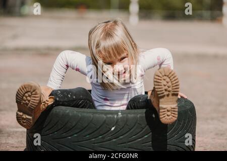 Dall'alto di felice adorabile bambina seduta all'interno dell'auto stanca mentre si diverte e si gioca all'aperto il giorno d'estate Foto Stock