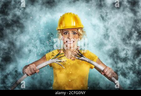 La ragazza lavoratrice con cappello rompe un cavo elettrico. Sfondo ciano Foto Stock