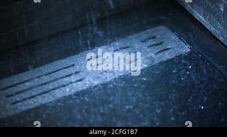 Da sopra torrenti di acqua che cadono sul pavimento e che scorre scarico in cabina doccia in bagno Foto Stock