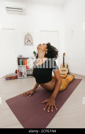 African American attraente giovane donna che esegue yoga posa con testa giù e mani gambe che si allungano sul tappeto in stanza leggera Foto Stock