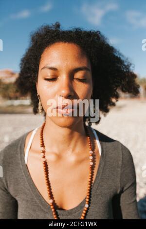 Primo piano ritratto di giovane donna afro-americana attraente meditare in spiaggia Foto Stock