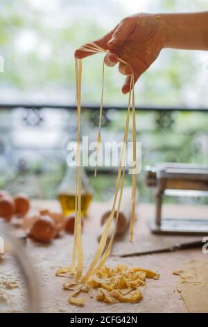 Donna che sta tagliando sottili strisce di pasta in mani mentre preparazione del pasto in cucina Foto Stock