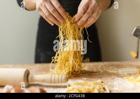 Donna che sta tagliando sottili strisce di pasta in mani mentre preparazione del pasto in cucina Foto Stock