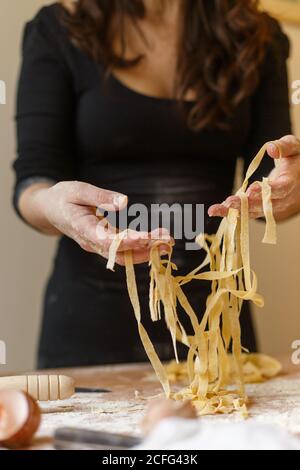 Donna che sta tagliando sottili strisce di pasta in mani mentre preparazione del pasto in cucina Foto Stock