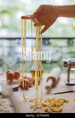 Donna che sta tagliando sottili strisce di pasta in mani mentre preparazione del pasto in cucina Foto Stock