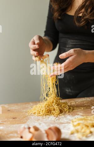 Donna che sta tagliando sottili strisce di pasta in mani mentre preparazione del pasto in cucina Foto Stock