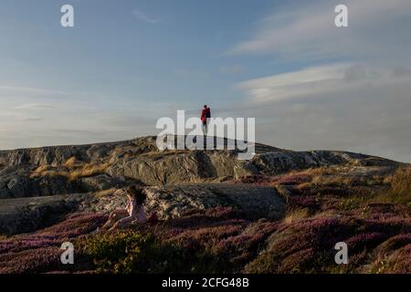 Vista sul retro di una coppia anonima di viaggiatori che camminano sulla roccia scogliera coperta di erba e fiori e ammirando il paesaggio pittoresco Foto Stock