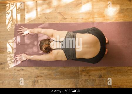 Dall'alto di calmo femmina in activewear che si allunga indietro e. fare esercizi di yoga sul tappetino in piano luminoso Foto Stock