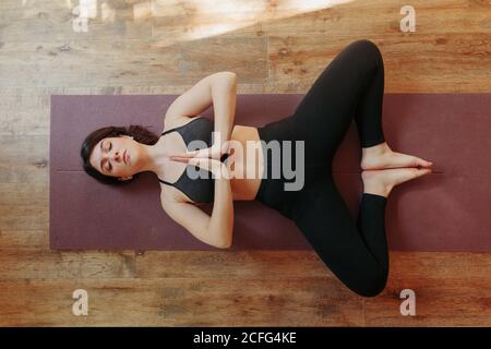 Dall'alto di calmo femmina in activewear che si allunga indietro e. fare esercizi di yoga sul tappetino in piano luminoso Foto Stock