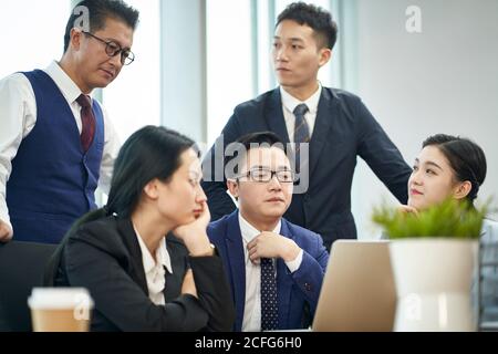 team di dirigenti aziendali asiatici che si riunono per discutere l'uso aziendale computer portatile Foto Stock