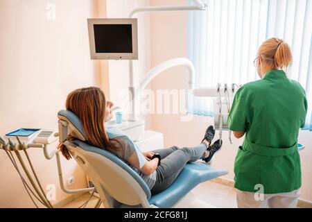 Messo a fuoco medico professionale di mezza età in uniforme verde esame della cavità orale di Donna in sedia dentista Foto Stock